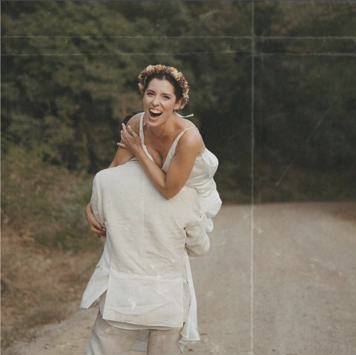 Novio llevando a la novia en el hombro sonriente y con una corona de flores.